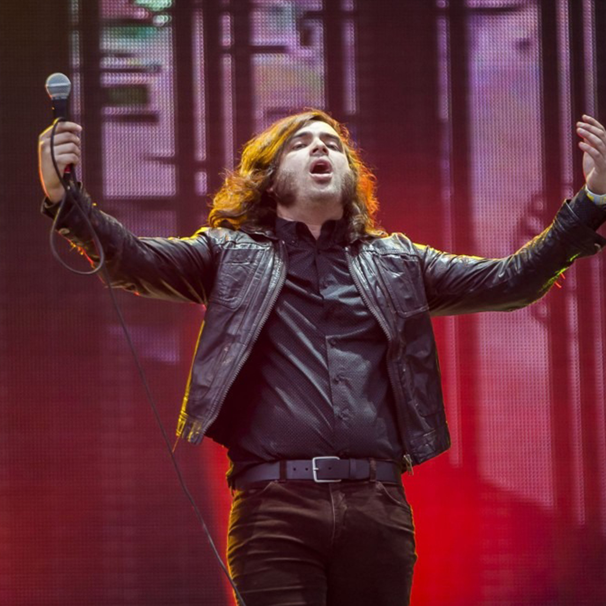 Luis Humerto Navejas, vocalista de enjambre en el escenario, mirando hacia el cielo con con los brazos extendidos y con micrófono en su mano derecho